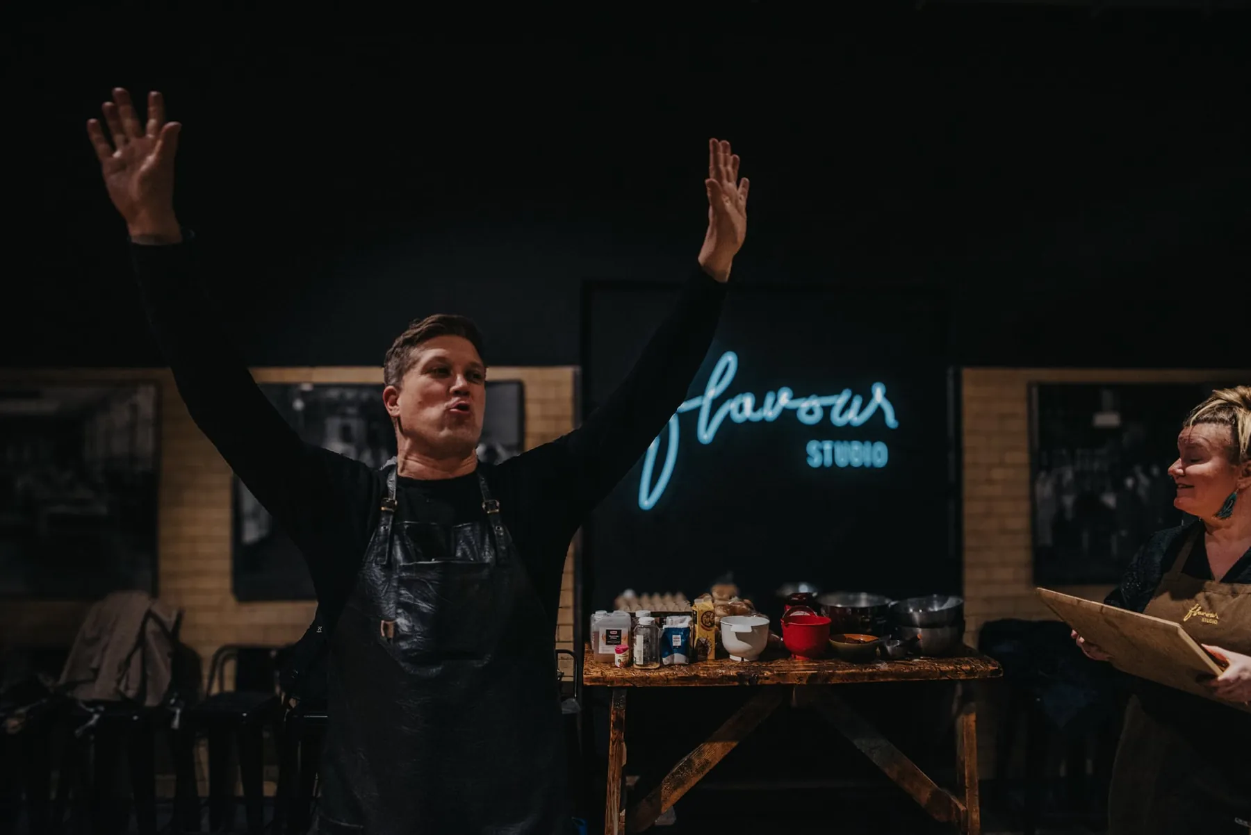 A chef with his arms up in front of the neon.